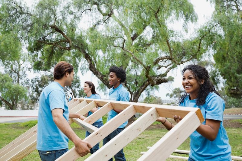 Un groupe de volontaires vêtus de chemises bleues soulèvent le cadre en bois d'un mur